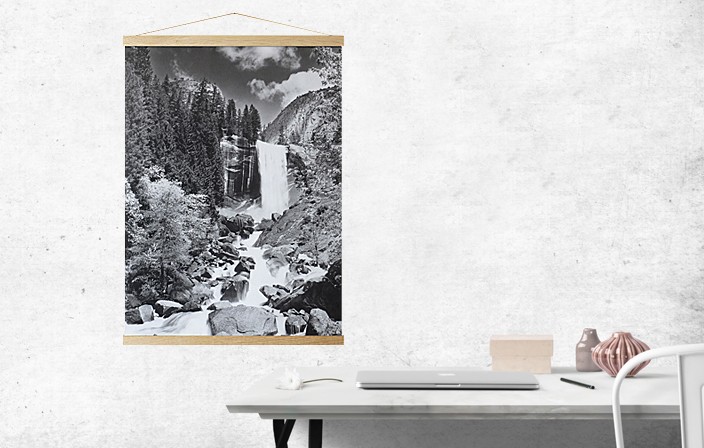 Oak wood Magnetic Poster Holder with poster of a mountain land with waterfall, hanging in interior with a desk. Picture frame producer Debex Suisse.
