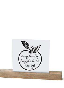 An apple a day keeps the doctor away quote on a white card in a wooden stand