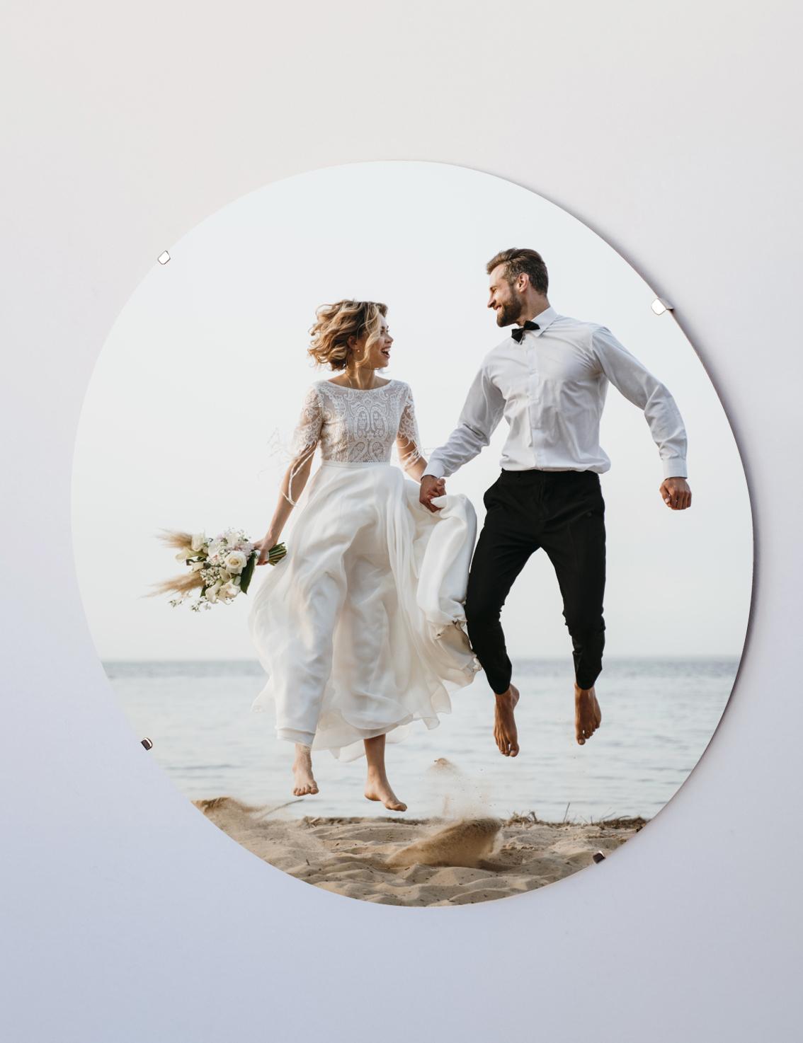 Newlywed couple jumping for joy on a sandy beach at sunset, framed in a circular print